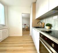 Dizajnový moderný 2 izbový byt Jurigovo nám. Bratislava IV Karlova Ves - Kuchyňa v 2-izbovom byte s bielymi skrinkami a podlahou s dreveným dekorom.