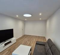 Prenájom 2-izbového bytu Bratislava II, Ružinov - Obývacia izba v 2-izbovom byte s pohovkou, televízorom a drevenou podlahou.