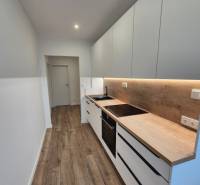 Prenájom 2-izbového bytu Bratislava II, Ružinov - Úzka kuchyňa v 2-izbovom byte s drevenou podlahou a bielymi skrinkami.