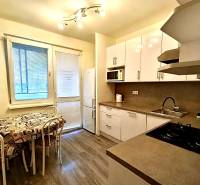 Predaj 4-izbového bytu na začiatku Petržalky Bratislava V - Kuchyňa v 4-izbovom byte s podlahou s dreveným dekorom, bielymi skrinkami a jedálenským kútom.
