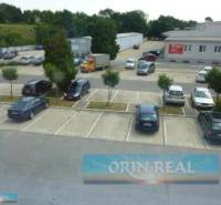 PRENÁJOM KANCELÁRSKÝCH PRIESTOROV NA RAČIANSKEJ ULICI - Parkovisko na ulici Račianska pri budove s kanceláriami, obklopené zeleňou a autami.