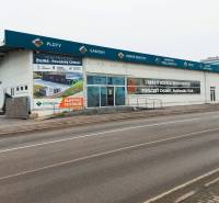 PRENÁJOM: Moderná hala (525 m²) v TOP lokalite Žiliny – Kamenná ul. - Obchodné priestory na Kamennej ulici v Žiline s reklamnými nápismi a prázdnym parkoviskom.