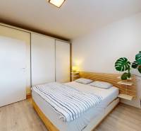 Na predaj 2-izbový byt v novostavbe s parkingom, Na pažiti, Trenčín - Spálňa v 2-izbovom byte s posteľou, skriňou a kvetom; podlaha s dreveným dekorom.