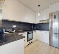 Na predaj 2-izbový byt v novostavbe s parkingom, Na pažiti, Trenčín - Kuchyňa v 2-izbovom byte s čiernymi pracovnými plochami a podlahou s dreveným dekorom.
