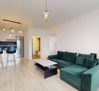 Na predaj 2-izbový byt v novostavbe s parkingom, Na pažiti, Trenčín - Kuchyňa v 2-izbovom byte s podlahou s dreveným dekorom, zelenou sedačkou a barovými stoličkami.