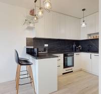 Na predaj 2-izbový byt v novostavbe s parkingom, Na pažiti, Trenčín - Kuchyňa v 2-izbovom byte s čiernym obkladom a podlahou s dreveným dekorom.