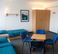 Na prenájom zrekonštruovaná ubytovňa s garážami a skladovacími kobkami - Izba s dvoma posteľami, modrá posteľná bielizeň, skriňa, stôl a štyri stoličky.