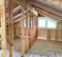 Chata pred dokončením, pozemok 770 m2, Horná Maríková - Podkrovie s oknom, drevenými trámami a podlahou s dreveným dekorom v chate.