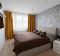 NOVINKA - Priestranných 74 m² v štýlovo zariadenom byte - Spálňa v 3-izbovom byte s podlahou s dreveným dekorom, šedou tapetou, žltými závesmi.