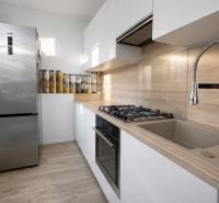 NOVINKA - Priestranných 74 m² v štýlovo zariadenom byte - Kuchyňa v 3-izbovom byte s lesklými skrinkami, nerezovou chladničkou a podlahou s dreveným dekorom.