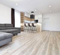 Na PRENÁJOM_v NOVOSTAVBE krásny 3-izbový byt s parkovacím státím - Obývačka v 3-izbovom byte s pohovkou, barom a podlahou s dreveným dekorom.