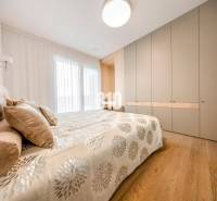 LUXUSNÝ 3-IZBOVÝ BYT NA MIERU V NADČASOVEJ NOVOSTAVBE NA ZAČIATKU KOLI - Spálňa v 3-izbovom byte s posteľou, vstavanou skriňou a podlahou s dreveným dekorom.