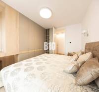 LUXUSNÝ 3-IZBOVÝ BYT NA MIERU V NADČASOVEJ NOVOSTAVBE NA ZAČIATKU KOLI - Spálňa v 3-izbovom byte s úložnými priestormi a posteľou so vzorovanými textíliami.