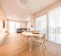 LUXUSNÝ 3-IZBOVÝ BYT NA MIERU V NADČASOVEJ NOVOSTAVBE NA ZAČIATKU KOLI - Obývacia izba v 3-izbovom byte s podlahou s dreveným dekorom, jedálenským stolom a sedačkou.