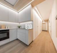 LUXUSNÝ 3-IZBOVÝ BYT NA MIERU V NADČASOVEJ NOVOSTAVBE NA ZAČIATKU KOLI - Kuchyňa v 3-izbovom byte s podlahou s dreveným dekorom a svetlým nábytkom.