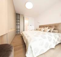 LUXUSNÝ 3-IZBOVÝ BYT NA MIERU V NADČASOVEJ NOVOSTAVBE NA ZAČIATKU KOLI - Svetlá spálňa s podlahou s dreveným dekorom a zabudovanými skriňami v 3-izbovom byte.