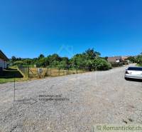 Stavebný pozemok pri Nitre so stavebným povolením v tichej lokalite - Pozemky - bývanie v Hosťovej: štrková cesta, oplotený pozemok, vedľa zaparkované auto.