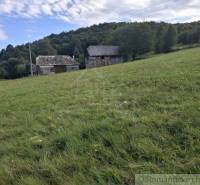 Veľký pozemok v srdci prírody pri Hornom Tisovníku - Trávnatý svah s budovami v pozadí, obklopený prírodou v Hornom Tisovníku, ideálny na Pozemky - bývanie.