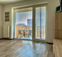 Na predaj moderný 2 izbový byt, komplex MIKO Trnava - Obývacia izba v 2-izbovom byte s podlahou s dreveným dekorom a prístupom na balkón.