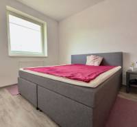 Na predaj moderný 2 izbový byt, komplex MIKO Trnava - Spálňa v 2-izbovom byte s posteľou, podlahou s dreveným dekorom a nočným stolíkom.