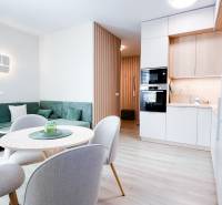 Na predaj 3 izbový byt s terasou, Trenčín, ul. Saratovská - Obývacia izba a kuchyňa v 3-izbovom byte s podlahou s dreveným dekorom a zeleným gaučom.