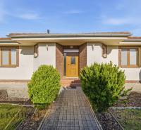 Na predaj 4-izb. rodinný dom s garážou, Kútniky - Rodinný dom v Kútnikoch s kríkovou výsadbou, bielou fasádou a hnedými doplnkami.