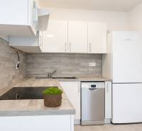 NOVOSTAVBA (2019) + PARKOVANIE | 2-izbový byt 69 m² – Bratislava - Kuchyňa s bielymi skrinkami, spotrebičmi a podlahou s dreveným dekorom v 2-izbovom byte.