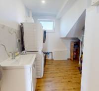 4-IZBOVÁ NOVOSTAVBA Horné Štitáre - Práčovňa s podlahou s dreveným dekorom, práčkou, sušičkou a umývadlom v rodinnom dome.