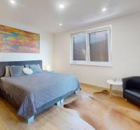 4-IZBOVÁ NOVOSTAVBA Horné Štitáre - Spálňa v rodinnom dome s posteľou, kreslom a podlahou s dreveným dekorom.