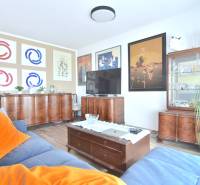 PRI VINOHRADOCH, 3-i byt s veľkými loggiami, 113 m2, RAČANY BIANCO - Obývačka v 3-izbovom byte s dreveným nábytkom, podlahou s dreveným dekorom a obrazmi na stenách.