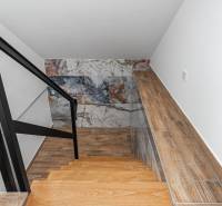I Predaj štýlového tehlového domu v Rajke pri Bratislave - Interiér rodinného domu so schodiskom, čiernym zábradlím a stenou s dekoratívnym vzorom.