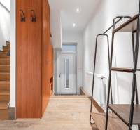 I Predaj štýlového tehlového domu v Rajke pri Bratislave - Chodba v rodinnom dome s podlahou s dreveným dekorom, bielymi stenami a dreveným schodiskom.