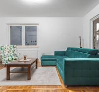 I Predaj štýlového tehlového domu v Rajke pri Bratislave - Obývacia izba so zelenou sedačkou, kreslom s motívom lístia a stolom, v rodinnom dome.