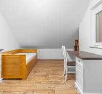 I Predaj štýlového tehlového domu v Rajke pri Bratislave - Podkrovná izba s posteľou, písacím stolom a podlahou s dreveným dekorom v rodinnom dome.