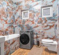 I Predaj štýlového tehlového domu v Rajke pri Bratislave - Kúpeľňa v rodinnom dome s farebnými kachľami, práčka, vaňa a záchod.