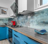 I Predaj štýlového tehlového domu v Rajke pri Bratislave - Kuchyňa s modrými skrinkami, červeným kávovarom a podlahou s dreveným dekorom.