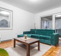 I Predaj štýlového tehlového domu v Rajke pri Bratislave - Obývačka v rodinnom dome s tyrkysovou sedačkou, kvetinovým kreslom a podlahou s dreveným dekorom.