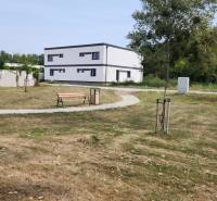 I Predaj 5-i mezonetu s vlastným pozemkom - Park s lavičkou a chodníkom, v pozadí budova v Dunajskom Klátove, 5 a viac izbový byt.