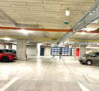 I Predaj 3i bytu v novostavbe v Rači - Podzemné parkovisko s parkovanými autami a pruhovanými stĺpmi, betónová konštrukcia, jasné osvetlenie.