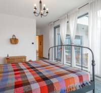 I PREDAJ moderná vila s bazénom a veľkým pozemkom - Spálňa s kovovou posteľou, pestrofarebným prehozom, závesmi a podlahou s dreveným dekorom v rodinnom dome.