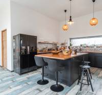 I PREDAJ moderná vila s bazénom a veľkým pozemkom - Kuchyňa vo vile s dreveným dekorom, čiernym nábytkom a centrálnym ostrovom.