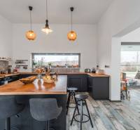 I PREDAJ moderná vila s bazénom a veľkým pozemkom - Kuchyňa vo vile s dreveným dekorom, barovými stoličkami a závesným osvetlením.