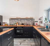 I PREDAJ moderná vila s bazénom a veľkým pozemkom - Kuchyňa vo vile s čiernymi skrinkami, dekoratívnym obkladom a podlahou s dreveným dekorom.