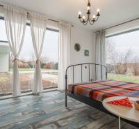 I PREDAJ moderná vila s bazénom a veľkým pozemkom - Spálňa vo vile s vysokými oknami, kovovou posteľou a podlahou s dreveným dekorom.