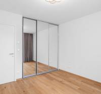 : Nadštandardný 2-i byt v projekte ZWIRN za cenu „štandardu“ - Izba v 2-izbovom byte s bielymi stenami, zrkadlovou skriňou a drevenou podlahou.