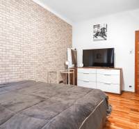I Na predaj 2-i byt s terasou v Auersthal (Rakúsko) - Spálňa s tehlovou tapetou, televízorom, komodou a podlahou s dreveným dekorom v 2-izbovom byte.