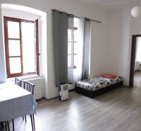 PRENÁJOM: HLAVNÁ - VOĽNÝ 2,5-izbový byt + kuchyňa, kúpeľňa, WC  - Obývacia izba so stolom a pohovkou v 3-izbovom byte, podlaha s dreveným dekorom.