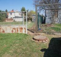 Pozemok v obci Koniarovce v slepej uličke - Brána vedúca na pozemok so stavbou a trávnatou plochou, ideálne pre bývanie.