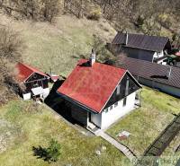 Chalupa - rodinný dom v krásnom prostredí – Moštenica, Banská Bystrica - Chata v Moštenici so šikmou červenou strechou, okolitá zeleň a svahovitý terén.