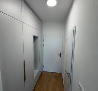 Garzónka v novostavbe AGÁTY, ul. Agátova, Dúbravka, lodžia  - Úzka chodba v garsónke s bielymi skriňami a podlahou s dreveným dekorom.